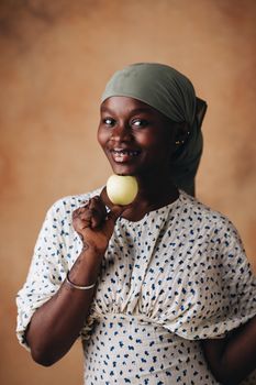 A cheerful woman in a headscarf holding an apple against a warm, artistic backdrop.