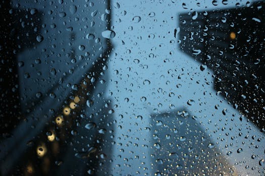 Raindrops on a window with blurred city buildings at night, capturing a moody urban scene.