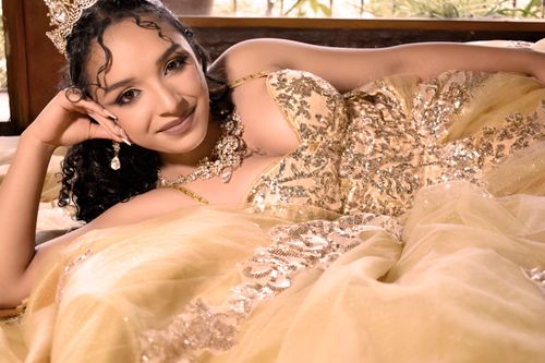 Free A woman in an elegant, golden gown with sparkling accents, posing gracefully indoors. Stock Photo