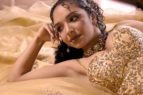 Free A woman lies gracefully in a sparkling golden gown, adorned with a tiara, exuding elegance and glamour. Stock Photo