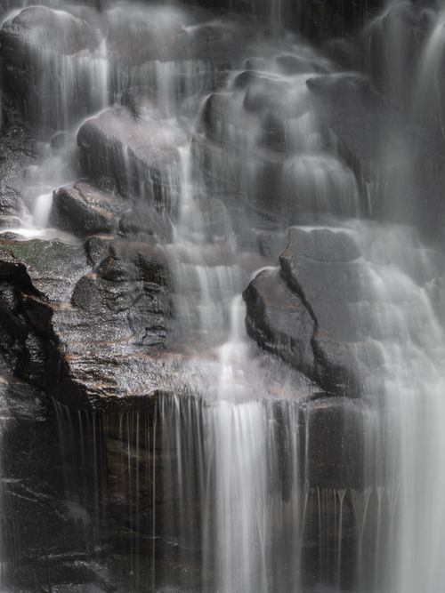 Free A tranquil waterfall gently cascading over textured rocks, captured in soft focus. Stock Photo
