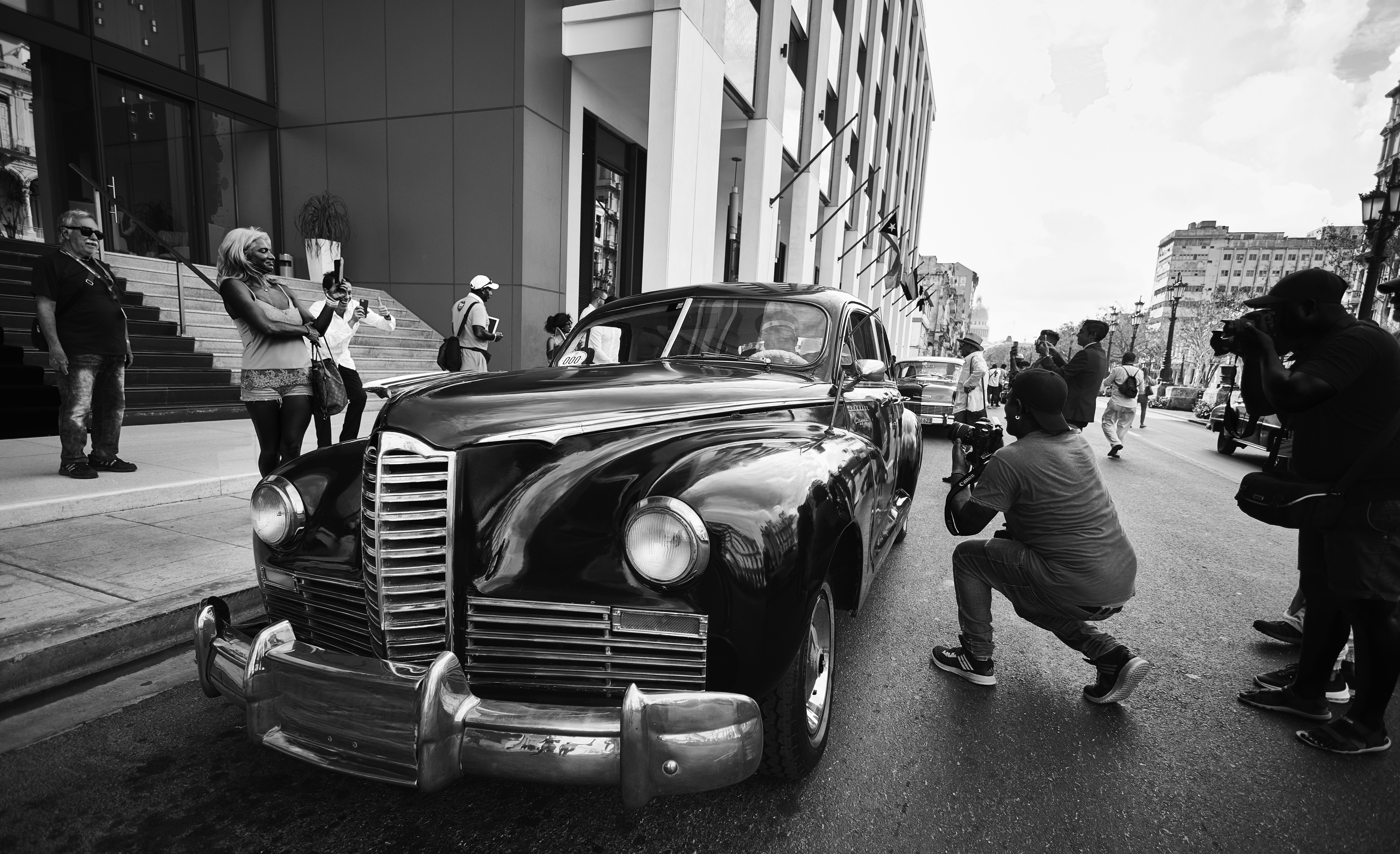 Photographers capturing vintage cars in an urban Havana street scene. Ideal for travel and cultural themes.