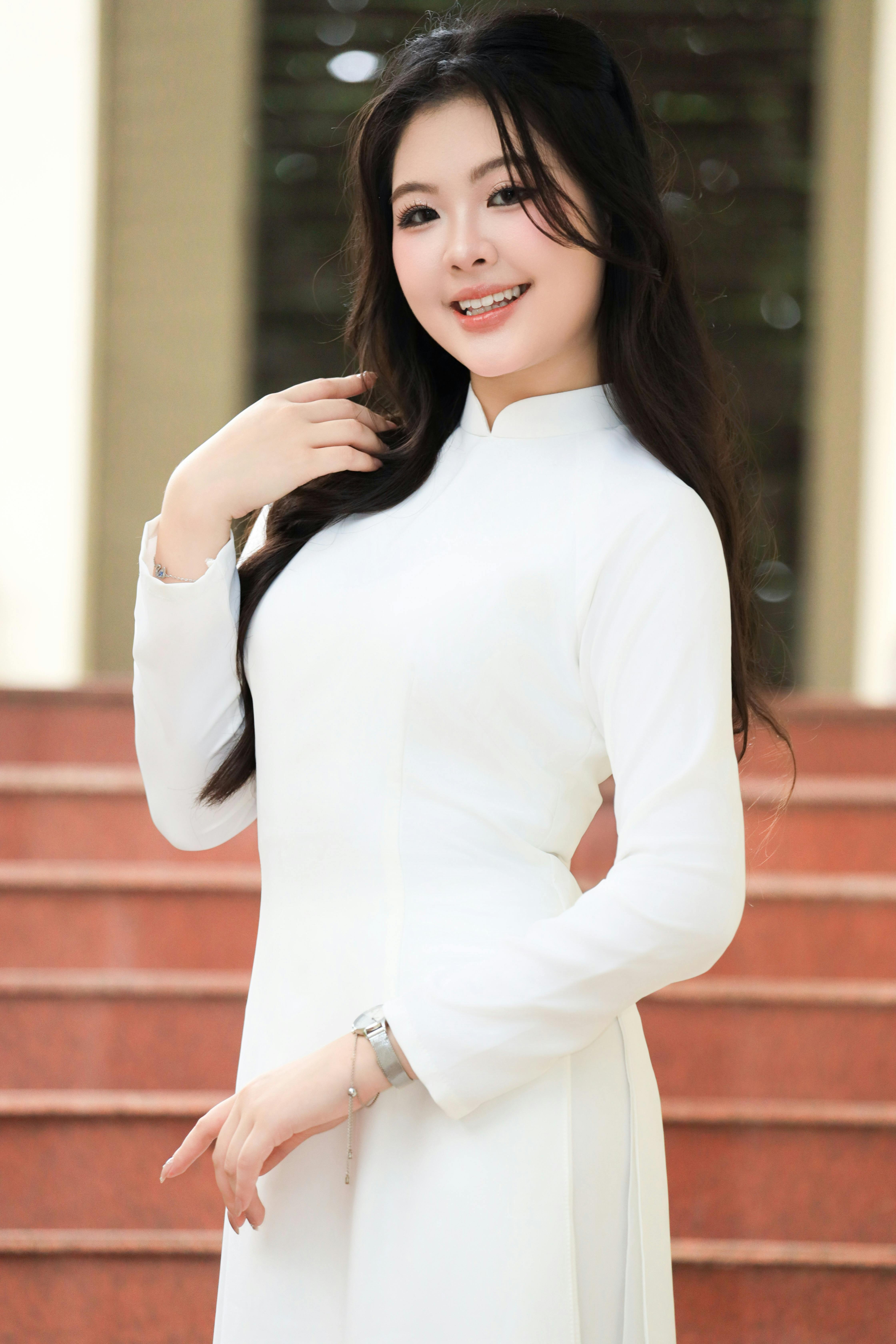 Portrait of a smiling Vietnamese woman in a traditional white Áo Dài, posing gracefully on steps.