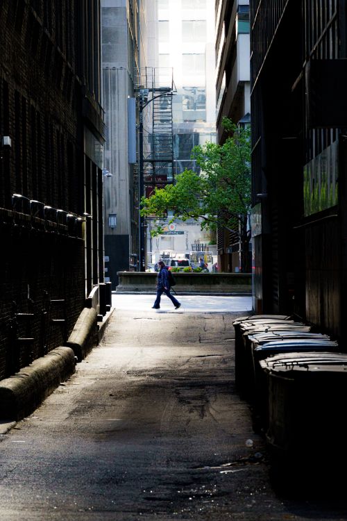 Free A lone person walks through a narrow urban alleyway in downtown Chicago, illuminated by sunlight. Stock Photo