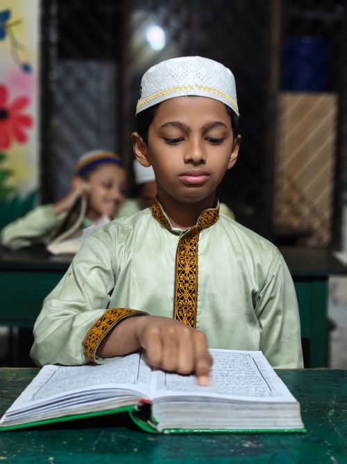 Free A young boy in traditional attire reads a religious book in a classroom setting. Stock Photo