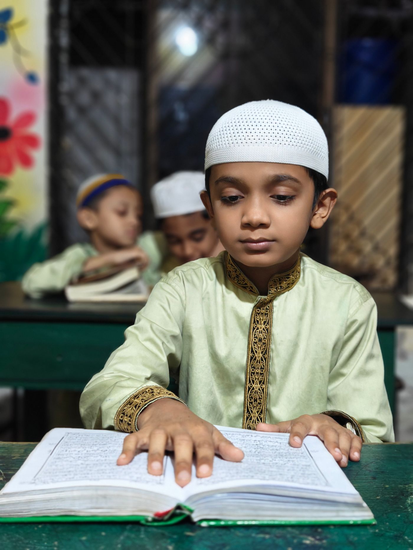 A young student reading the Quran attentively in a classroom