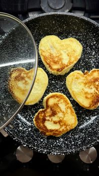 Heart-shaped pancakes cooked in a black speckled pan, perfect for breakfast aesthetics.