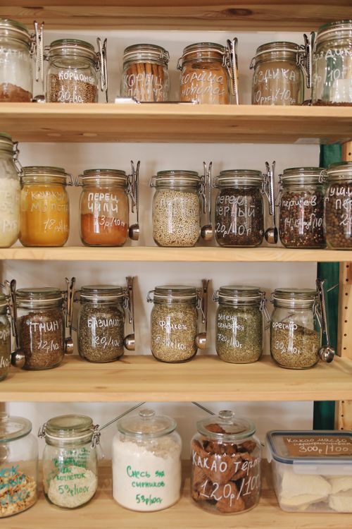 Free Glass jars filled with various spices and ingredients on wooden shelves promoting zero waste lifestyle. Stock Photo