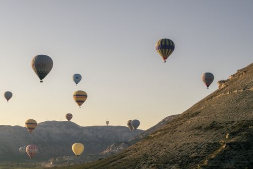 Free Scenic view of colorful hot air balloons floating over Cappadocia's rocky terrain at sunrise. Stock Photo