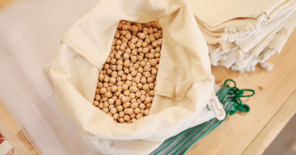 person filling a reusable bag with bulk grains and nuts at a market