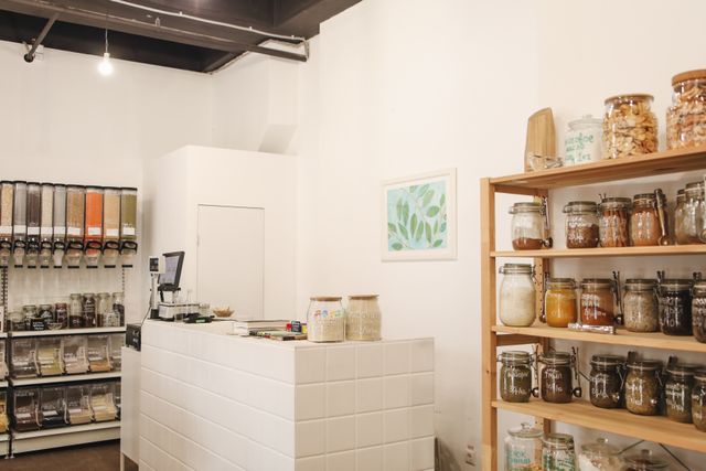 Refill shop interior with wooden shelves of clamp-lid jars and bulk dispensers. Photo by Polina Tankilevitch on Pexels.