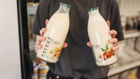 Person holding bottles of almond and soy milk substitutes in a store.