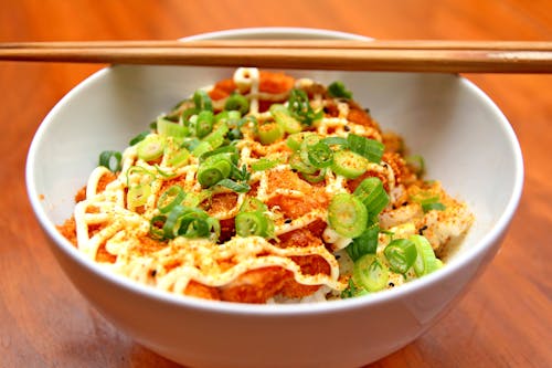 Brown Wooden Chopsticks on White Ceramic Bowl with Pork Cutlet and Spring Onion on Brown Wooden Table