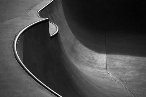 Free Dramatic shadows cast over smooth, curved concrete skatepark ramps in monochrome. Stock Photo