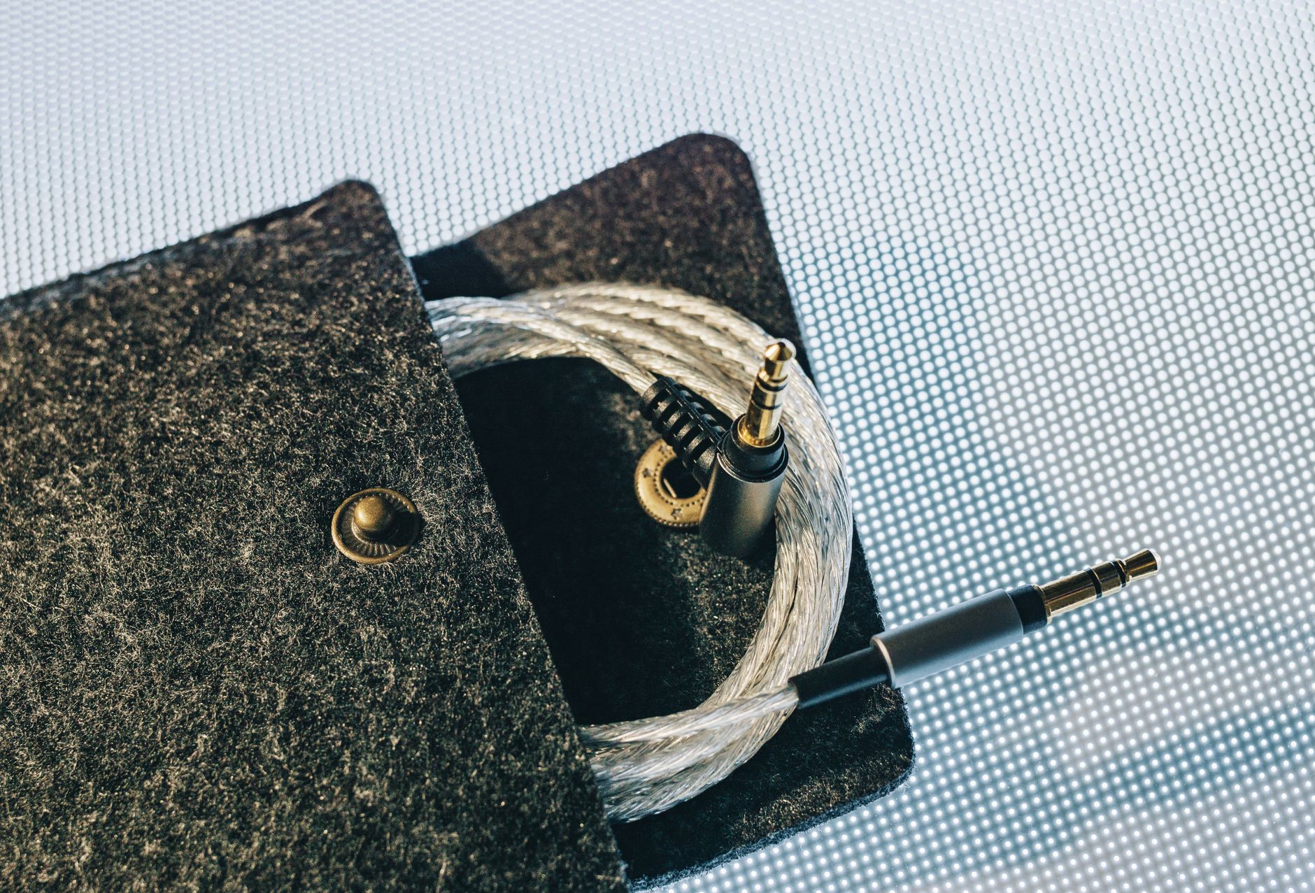 Detailed view of an audio cable coiled inside a soft felt pouch on a textured surface.