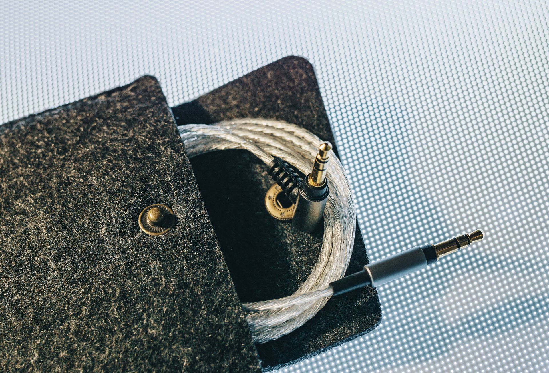 Detailed view of an audio cable coiled inside a soft felt pouch on a textured surface.