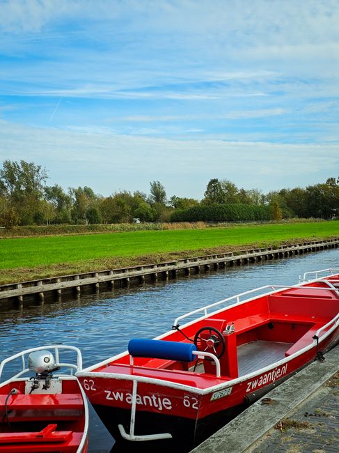 Picturesque red boat in Giethoorn's serene canal, with lush green surroundings on a clear day.