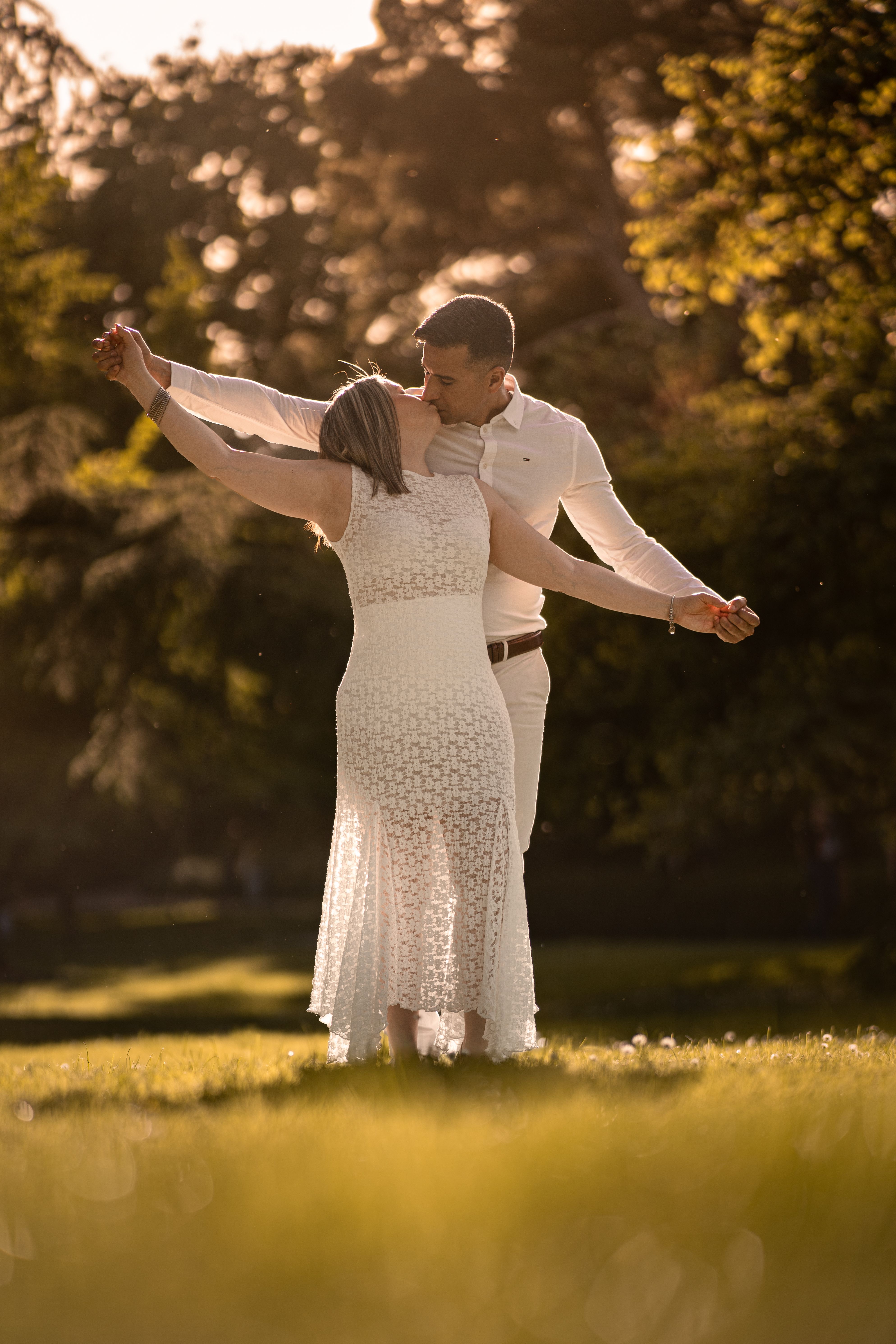 A couple dances gracefully in a sunlit park, captured with a warm and romantic atmosphere.