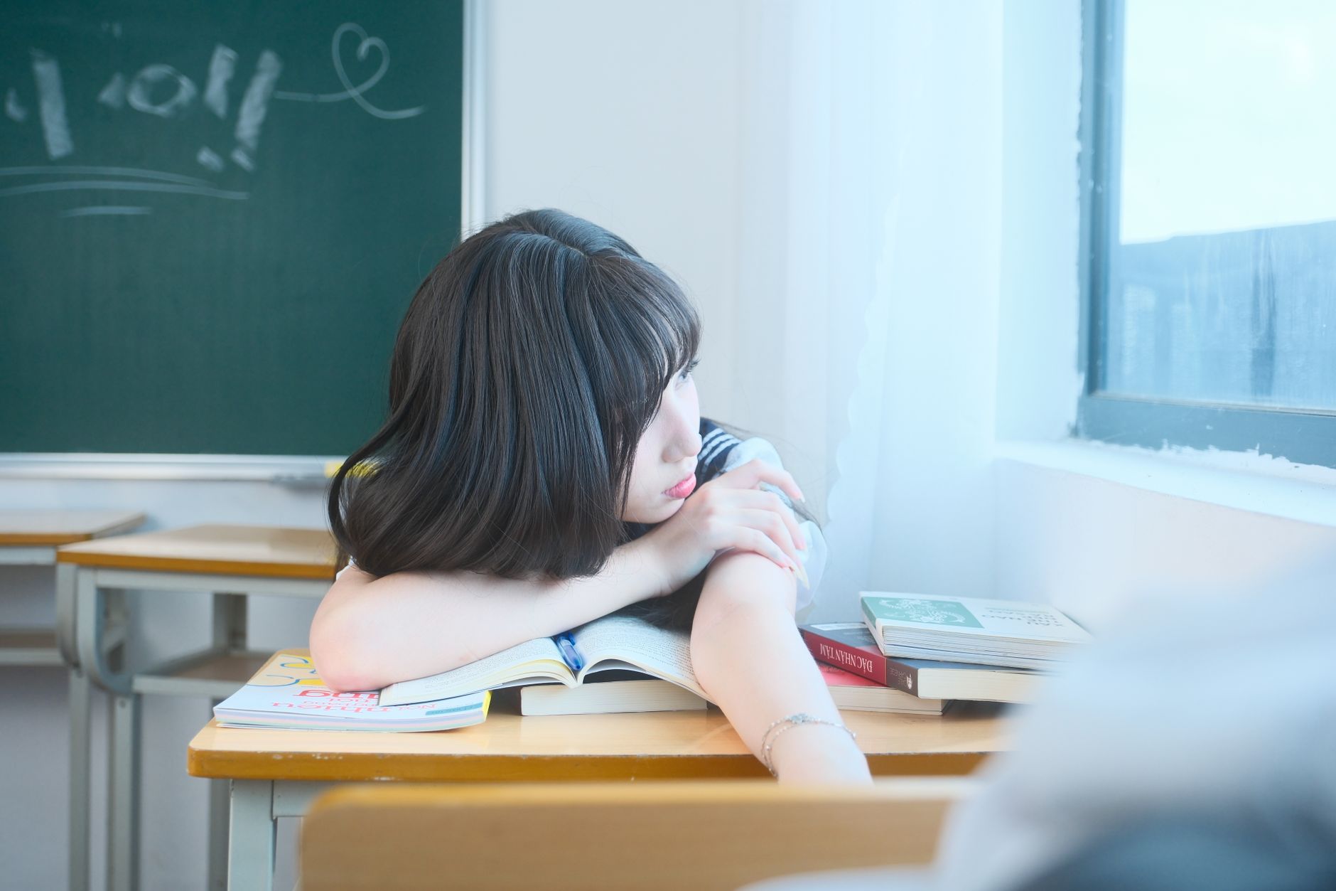 A student daydreaming beside the window in a Vietnamese classroom, surrounded by books.