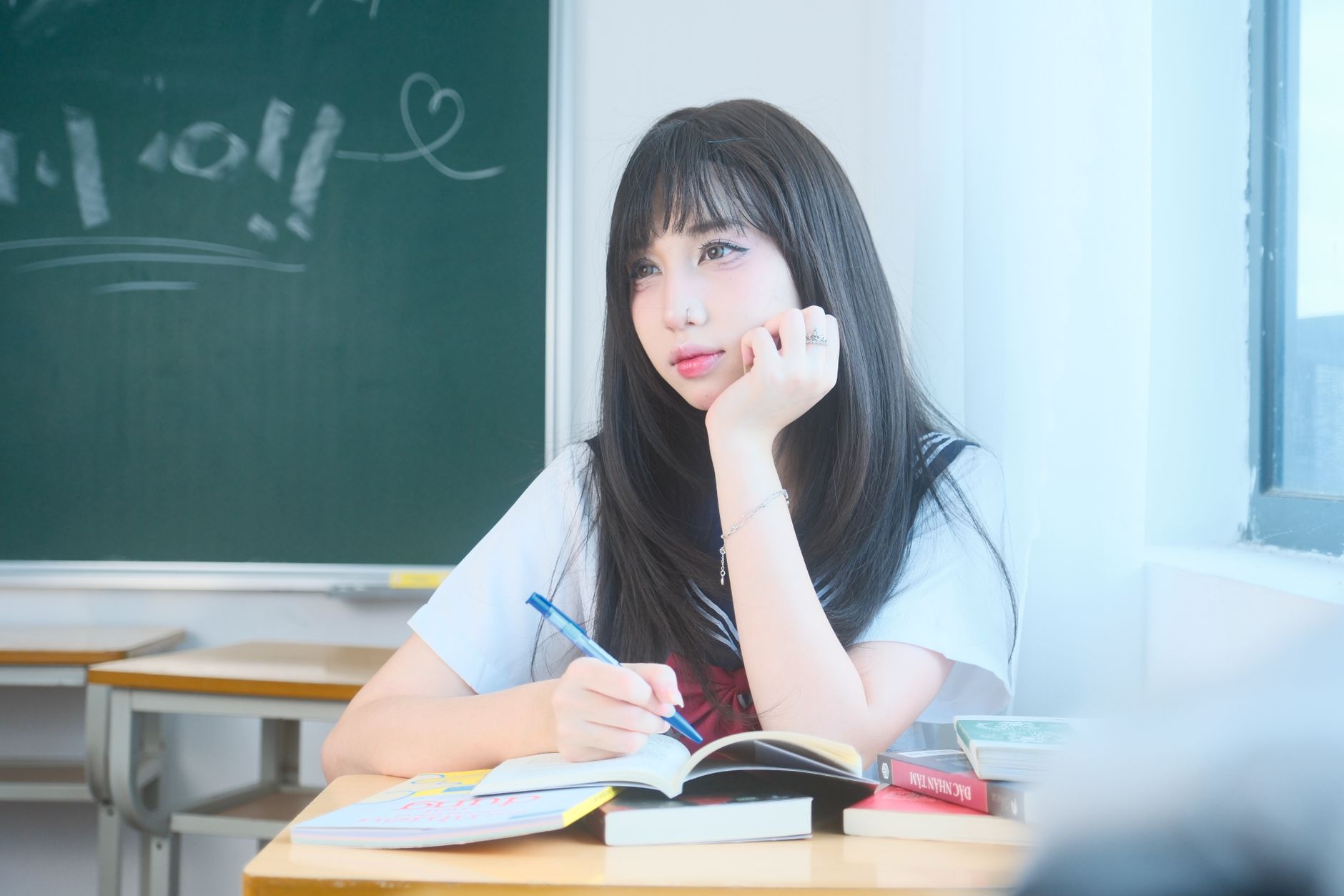 Thoughtful young woman sitting by window, studying with open books on desk in bright classroom.
