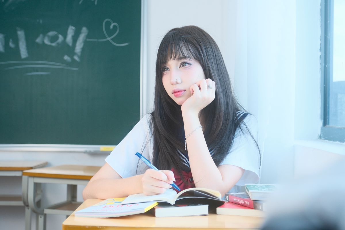 Thoughtful young woman sitting by window studying with open books