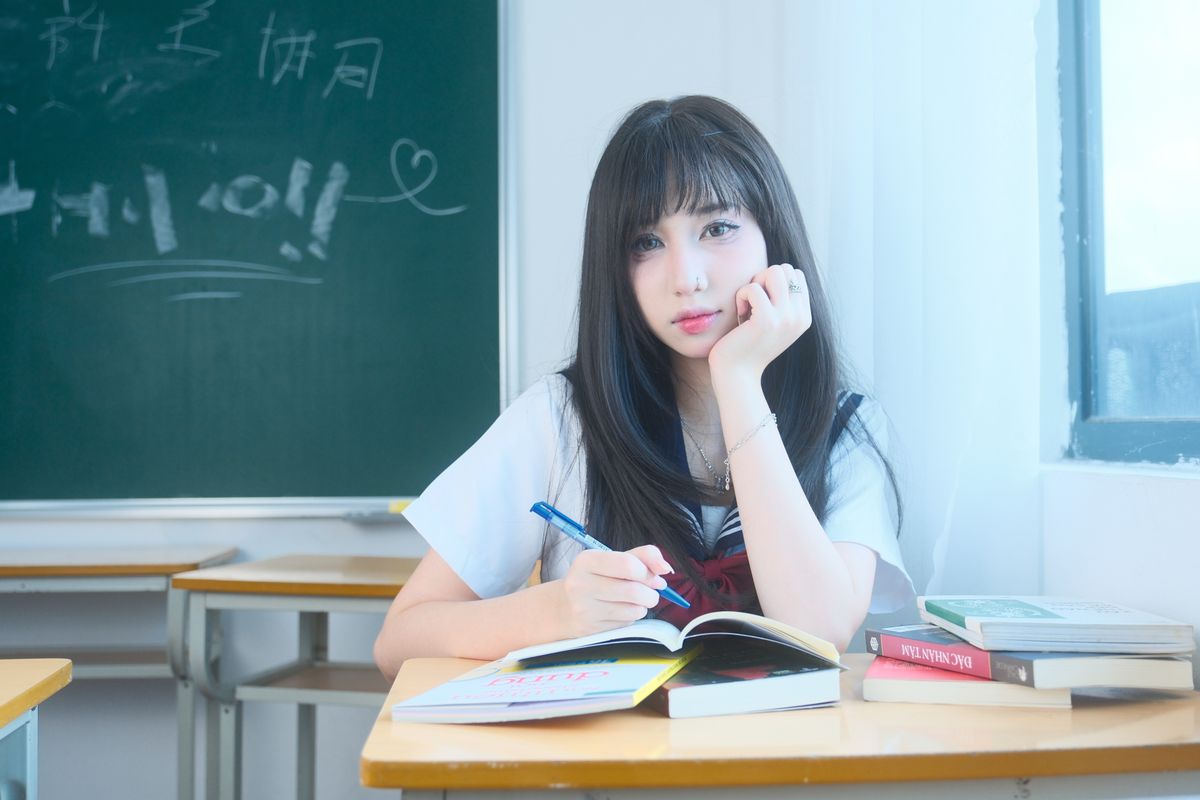 Young female student writing in notebook inside classroom