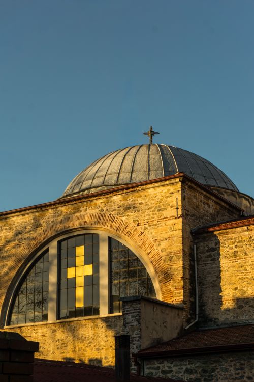 Free A beautifully lit historic church with a cross on a dome against a clear sky at sunset. Stock Photo