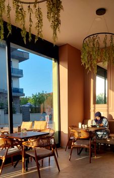 A serene cafe interior with a lone person reading by the window. Sunlight and decor add warmth.
