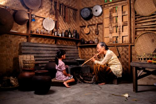 Free An elderly woman playing a flute for a young girl in a traditional Indonesian setting. Stock Photo