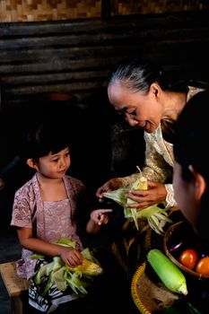 A heartwarming scene of a grandmother and child preparing corn together in an indoor setting in Indonesia. - Fotografer Sidoarjo