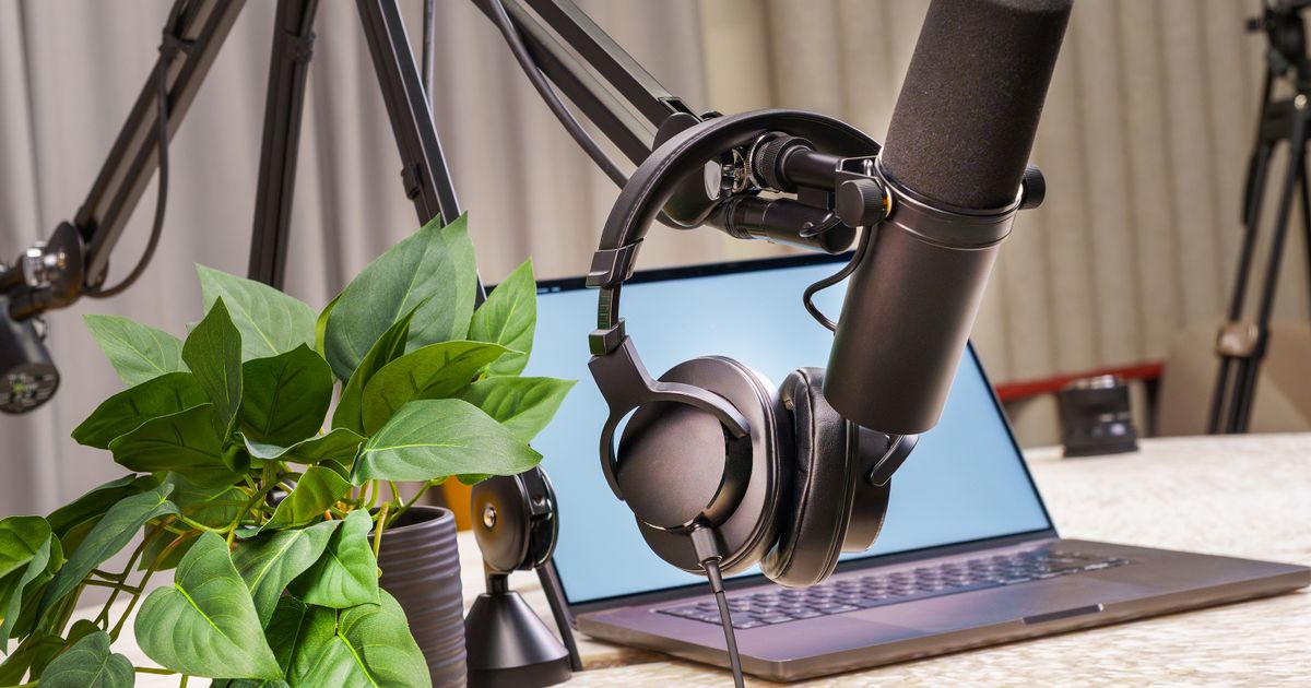 A podcast microphone on a boom arm beside headphones and a laptop