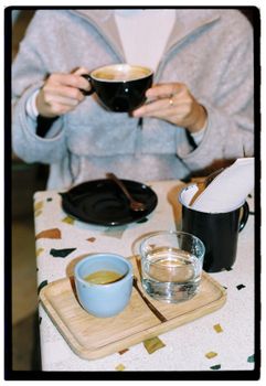 Person enjoying coffee in a cozy cafe with snacks on table.