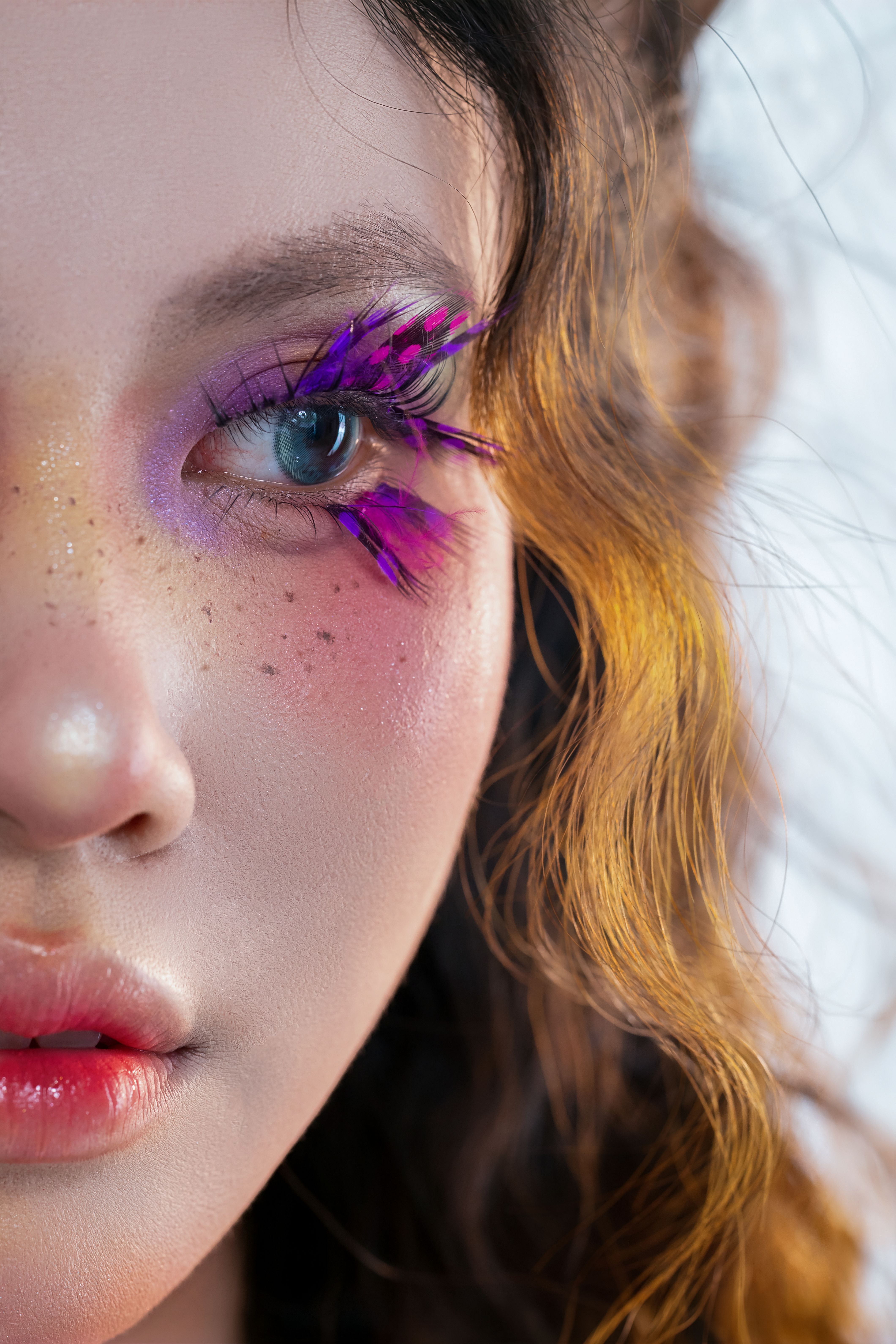 Vivid close-up of a woman with colorful eye makeup and detailed freckles.
