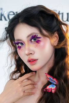 Close-up portrait featuring bold makeup and colorful butterfly accessory on young woman.