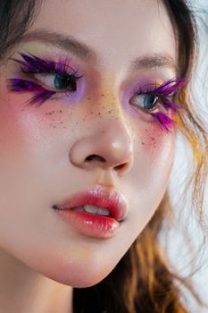 Vibrant close-up portrait of woman with creative colorful makeup and purple eyelashes.