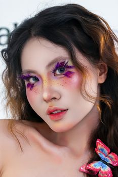 Vibrant portrait of a woman with artistic makeup and a butterfly accessory, showcasing colors and creativity.
