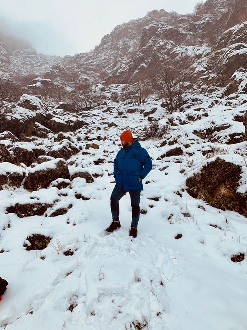 Free A person in a blue jacket stands on a snowy mountain slope, surrounded by rocky terrain and bare trees. Stock Photo