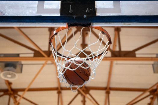 Close-up of a basketball going through a hoop inside a gym.