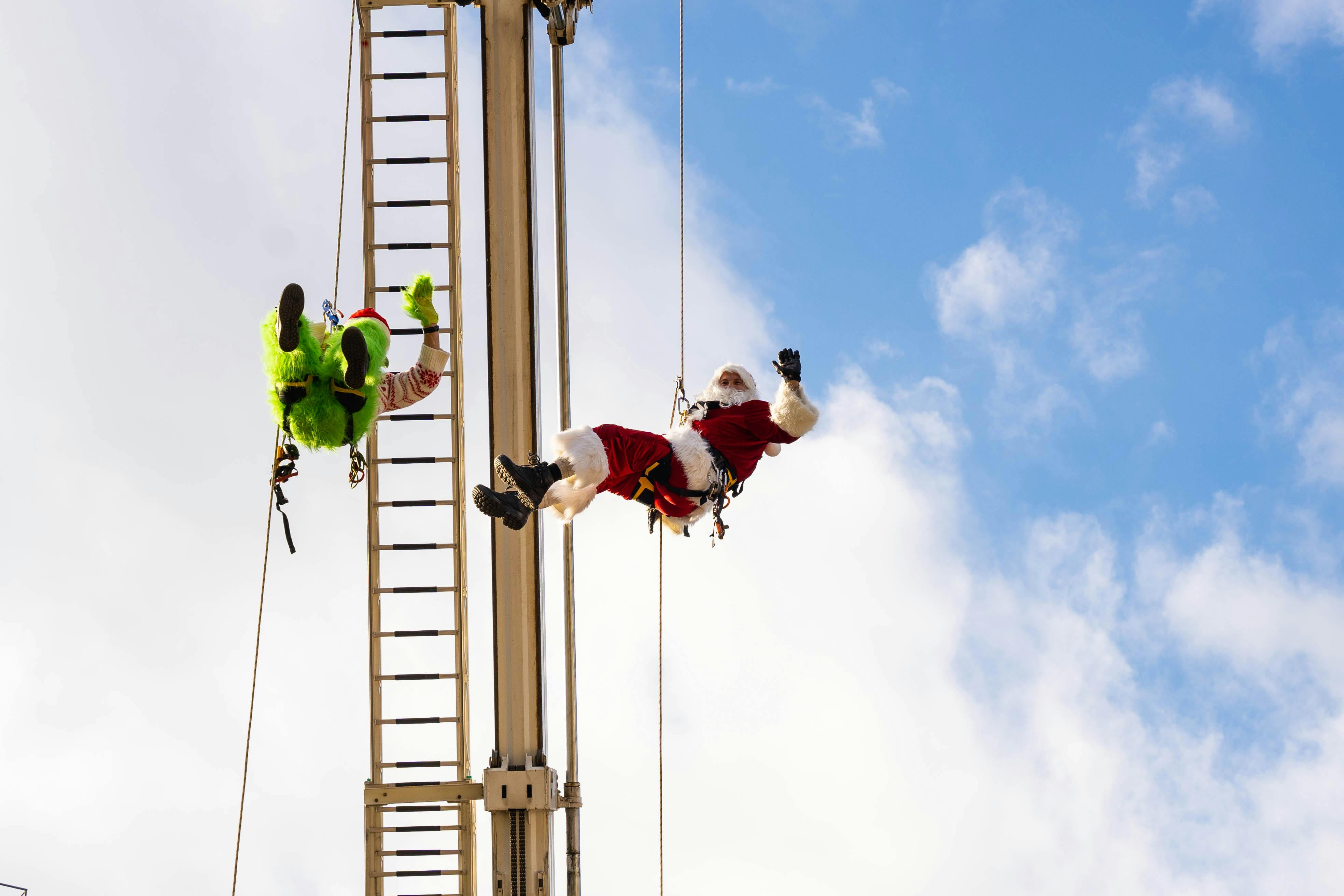 Santa Claus and the Grinch enjoying a fun climbing adventure against a bright blue sky.