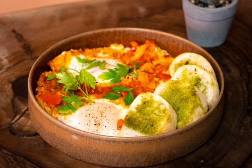 Free A vibrant bowl of shakshuka with fresh herbs and bread on a rustic wooden table. Stock Photo