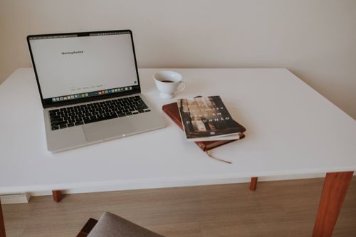 Free A clean, minimalist workspace with a laptop, book, and coffee on a white table. Stock Photo