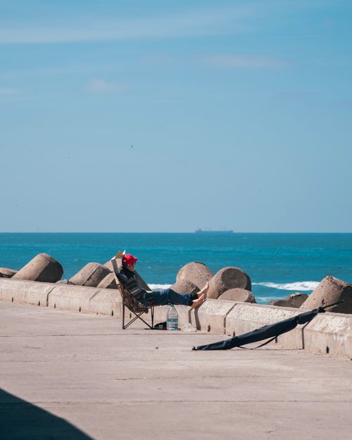 Free Person relaxing on a chair by the ocean on a sunny day. Tranquil beach scene. Stock Photo