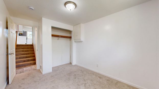 Spacious empty room with carpet, open closet, and stairs leading upwards.