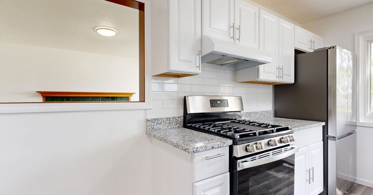 Bright white kitchen featuring stainless steel stove and fridge with granite countertops.