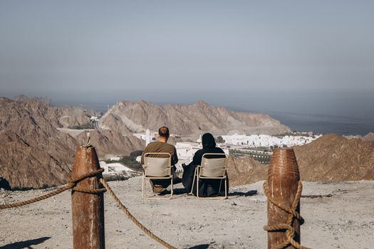 Two travelers enjoy the stunning mountain and city view from a hilltop in Nizwa, Oman.