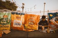 A young street vendor selling potato chips bags in Nizwa during sunset.