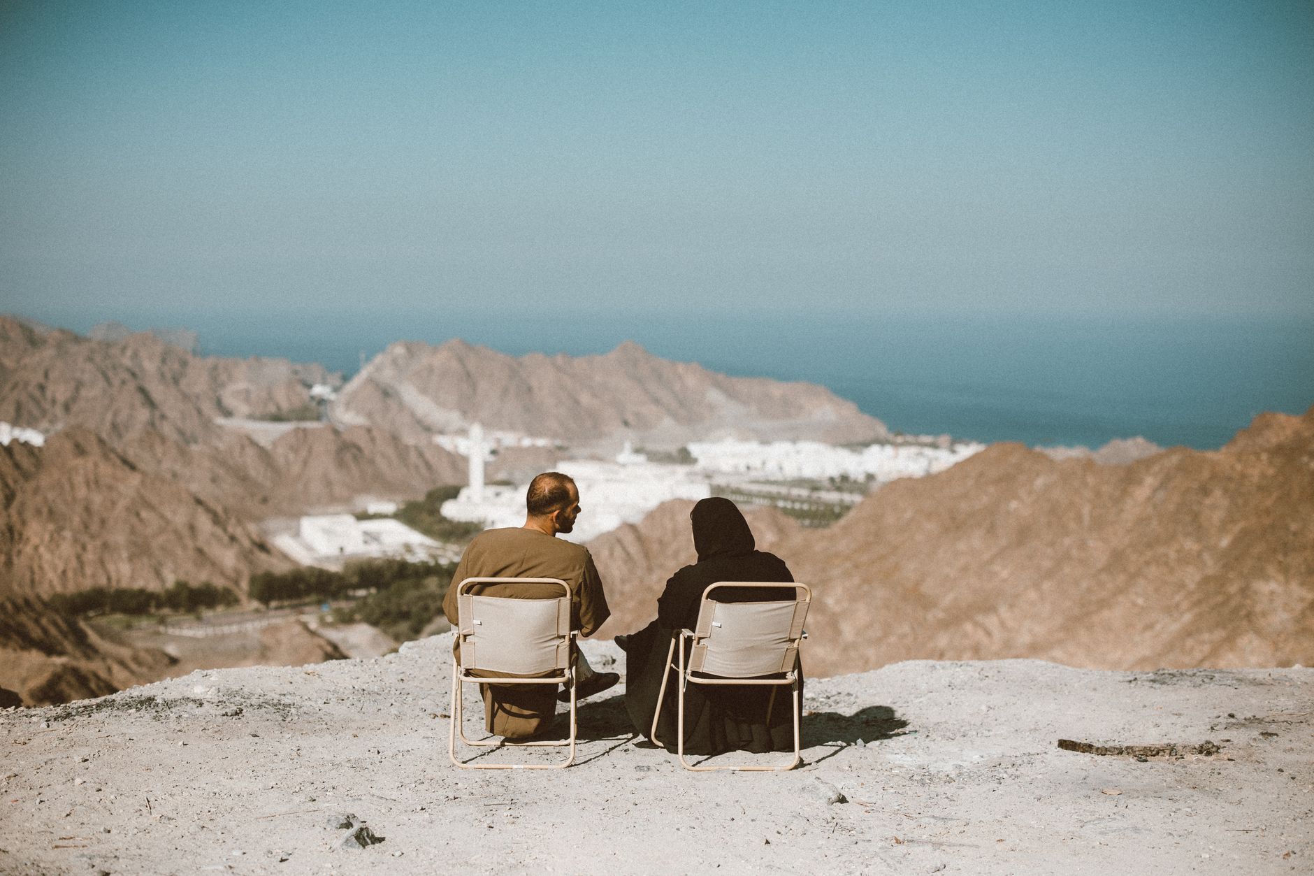 Two people enjoy a serene view over the mountains in Nizwa, Oman, capturing the essence of travel and tranquility.