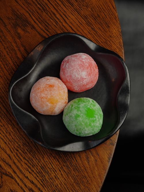 Free Three colorful mochi desserts on a black plate, showcasing vibrant flavors. Stock Photo