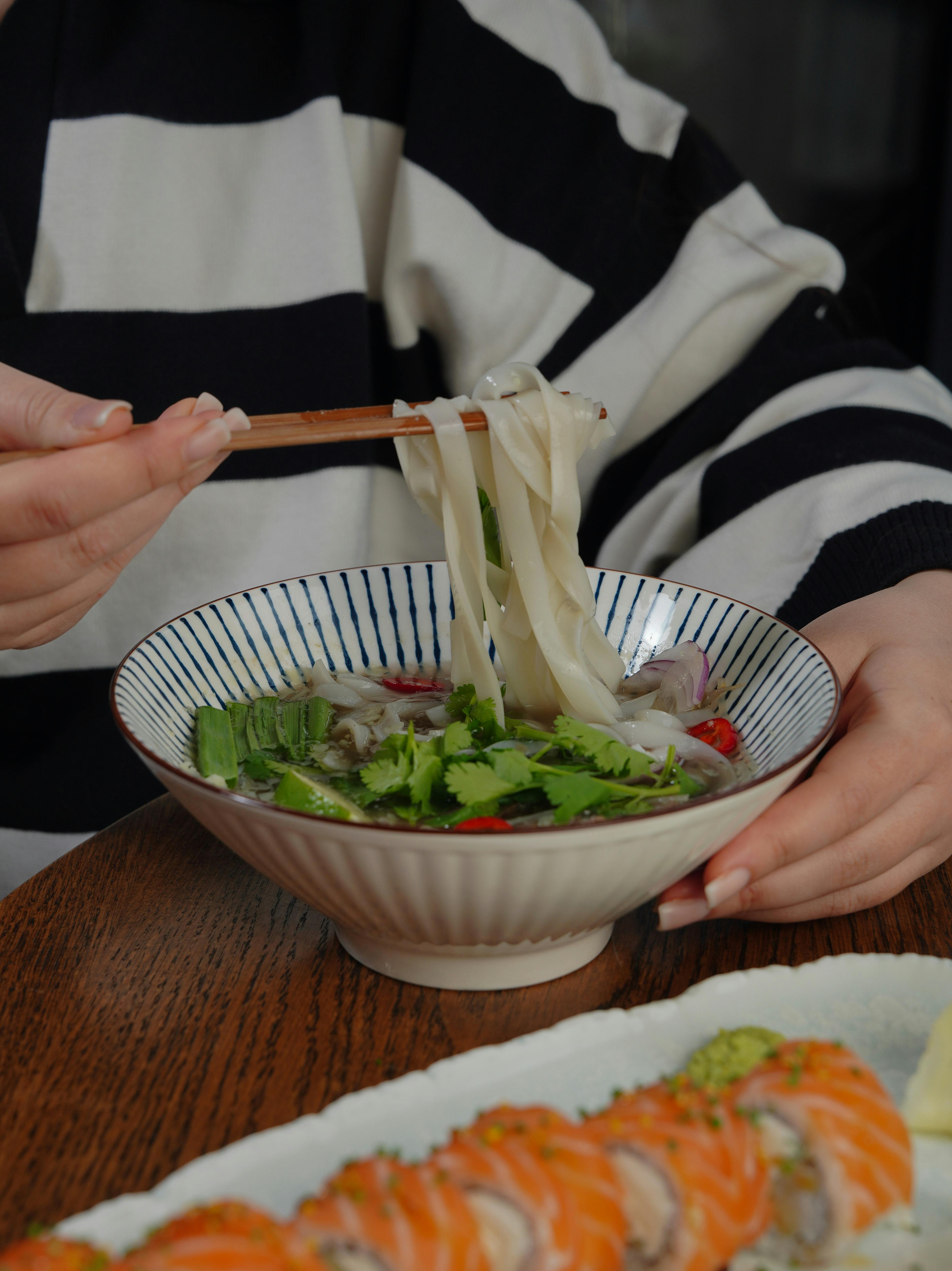 A person enjoying a bowl of Vietnamese pho noodle soup with sushi rolls. Perfect blend of Asian cuisines for food lovers.