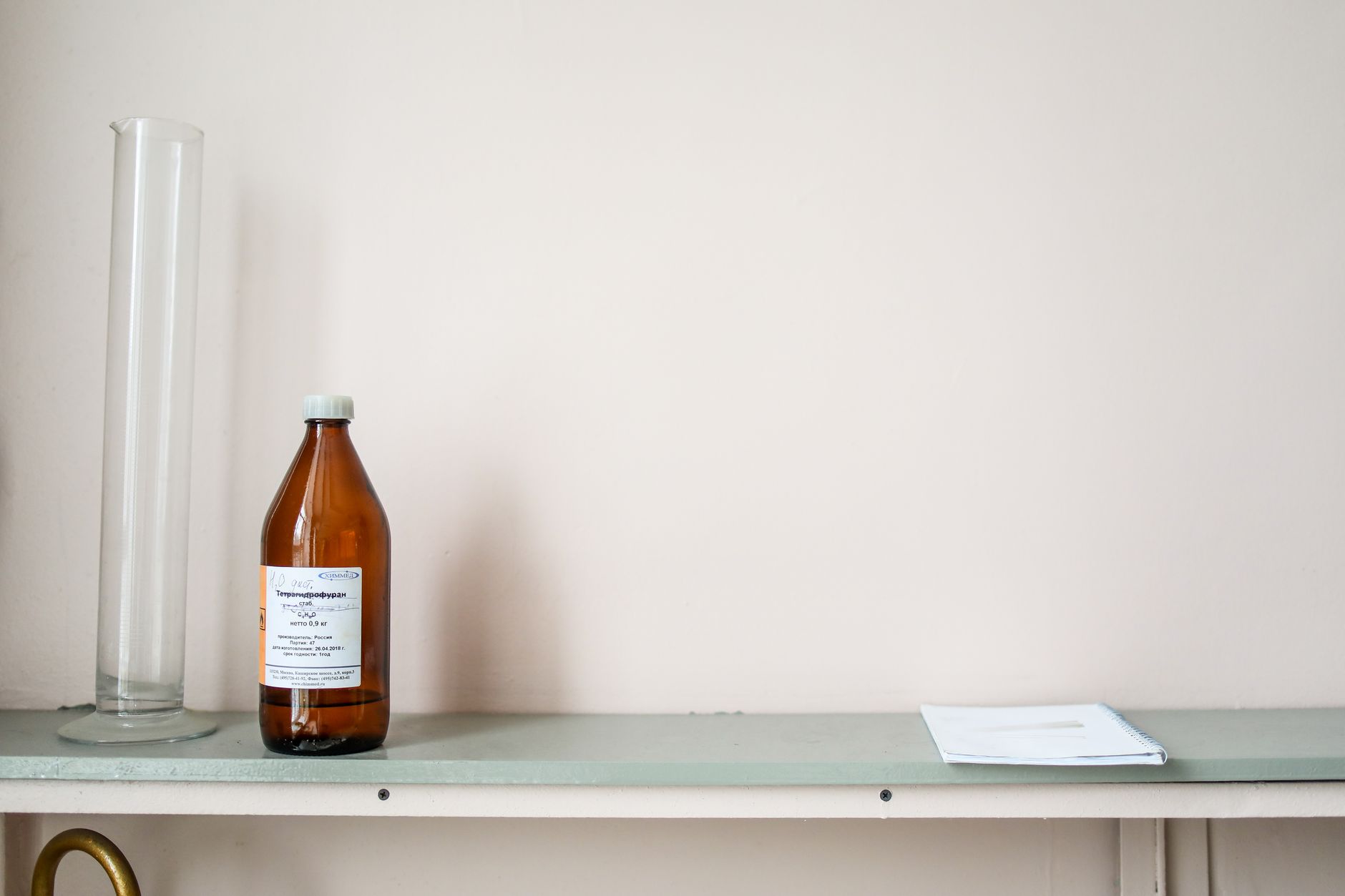 A minimalist laboratory setup with a chemical bottle and a glass cylinder on a shelf.